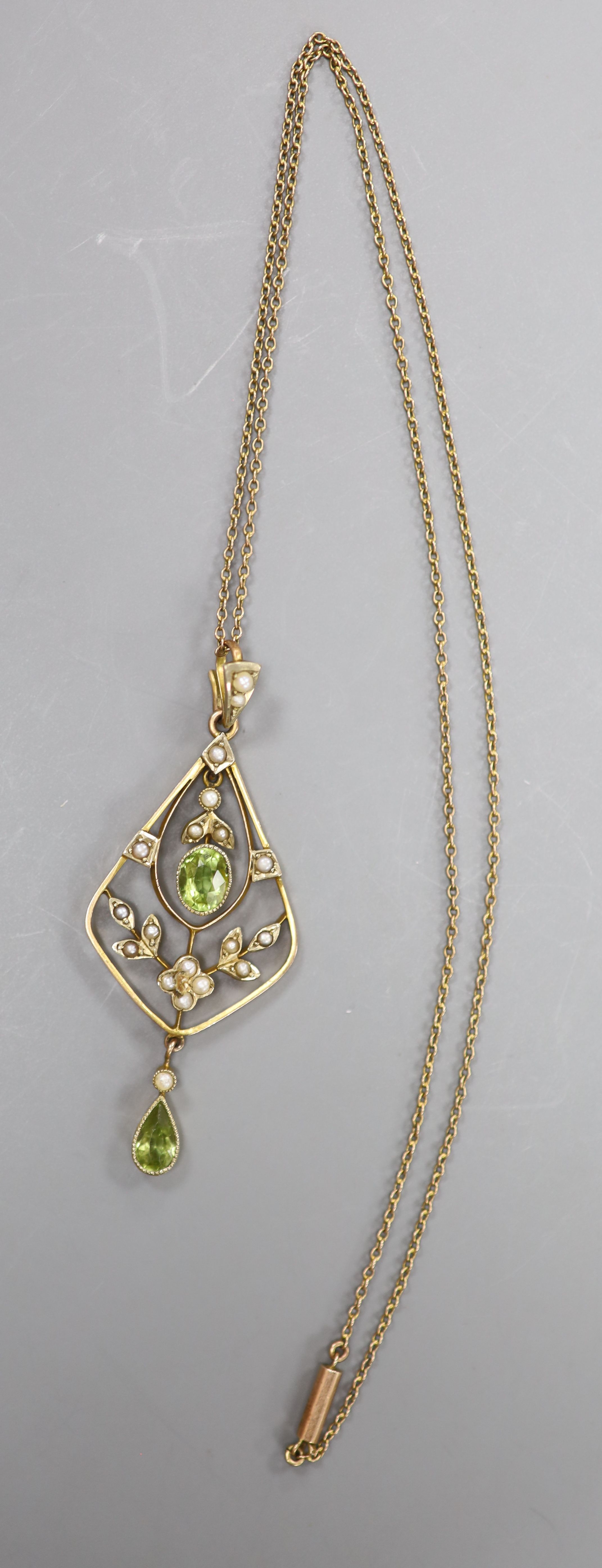 An early 20th century 9ct, peridot and seed pearl set drop pendant, 54mm, on a fine link yellow metal chain, 42cm